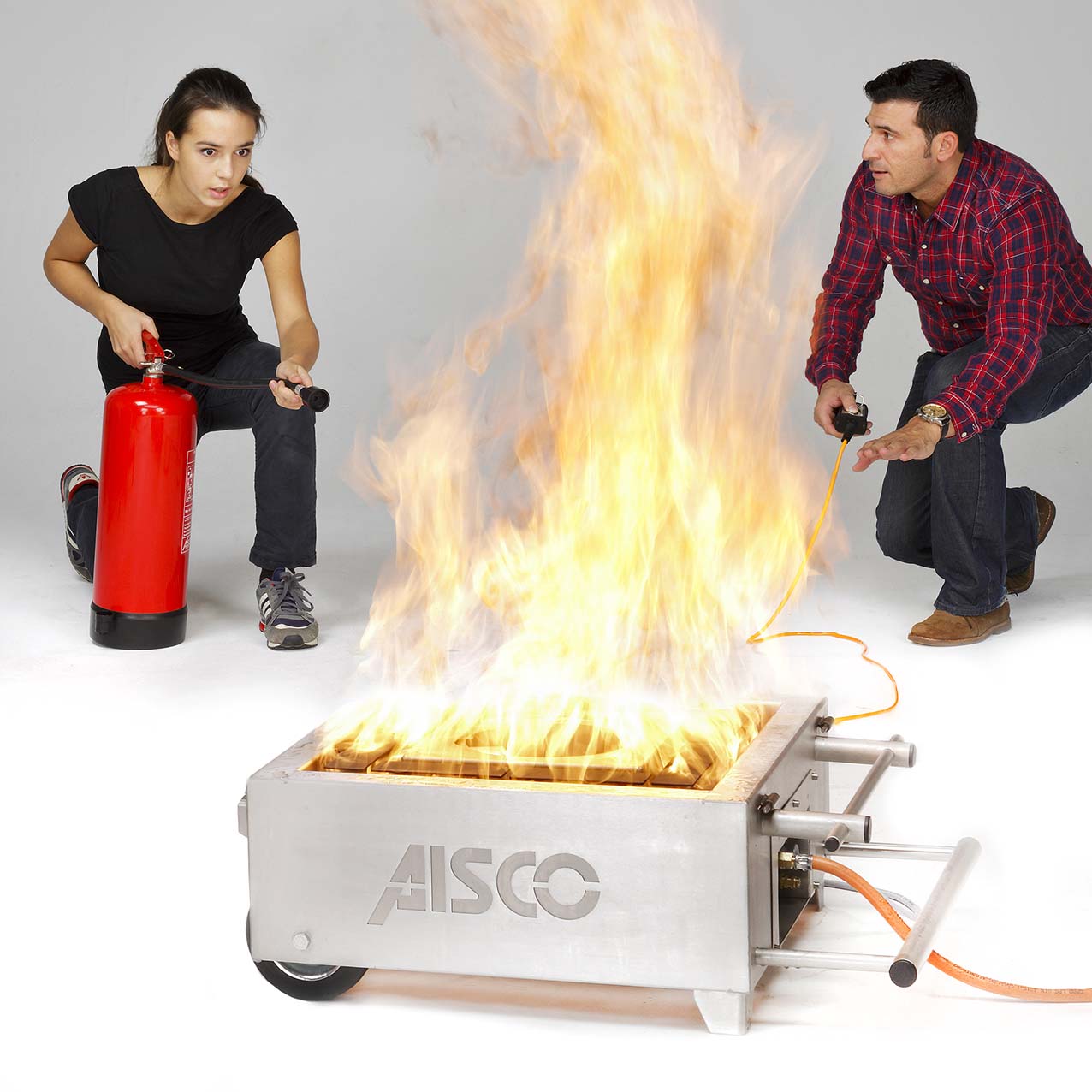 Eine Person löscht einen Flächenbrand am AISCO Firetrainer Caddy M, während der Brandschutzunterweiser daneben wertvolle Anweisungen und Unterstützung bei der Übung gibt