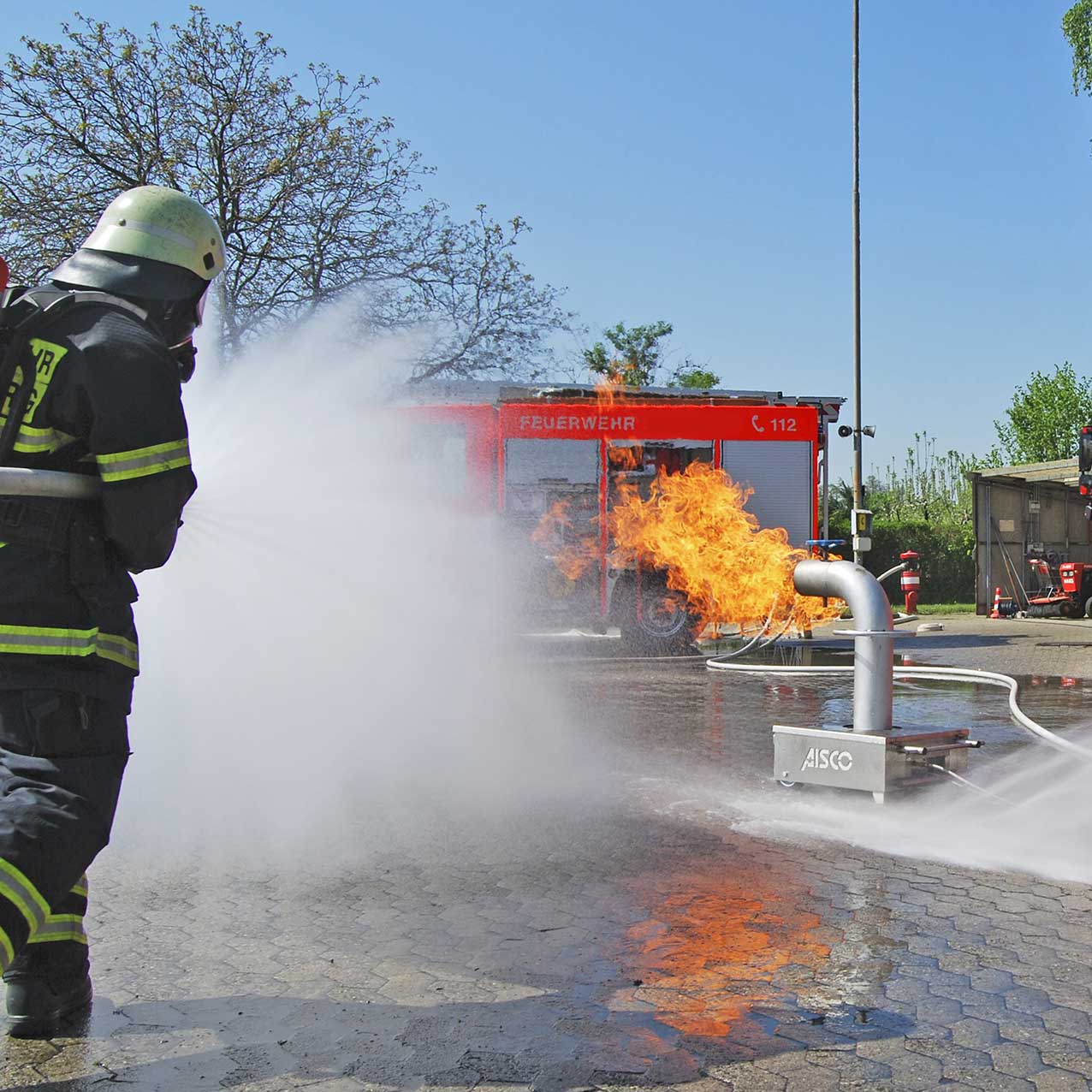 Feuerwehrmänner führen ein Hohlstrahlrohrtraining durch, um das Feuer zu löschen, während sie den AISCO Firetrainer Caddy M mit Industrieventil benutzen. Teamarbeit bei der Brandschutzübung mit professionellem Equipment