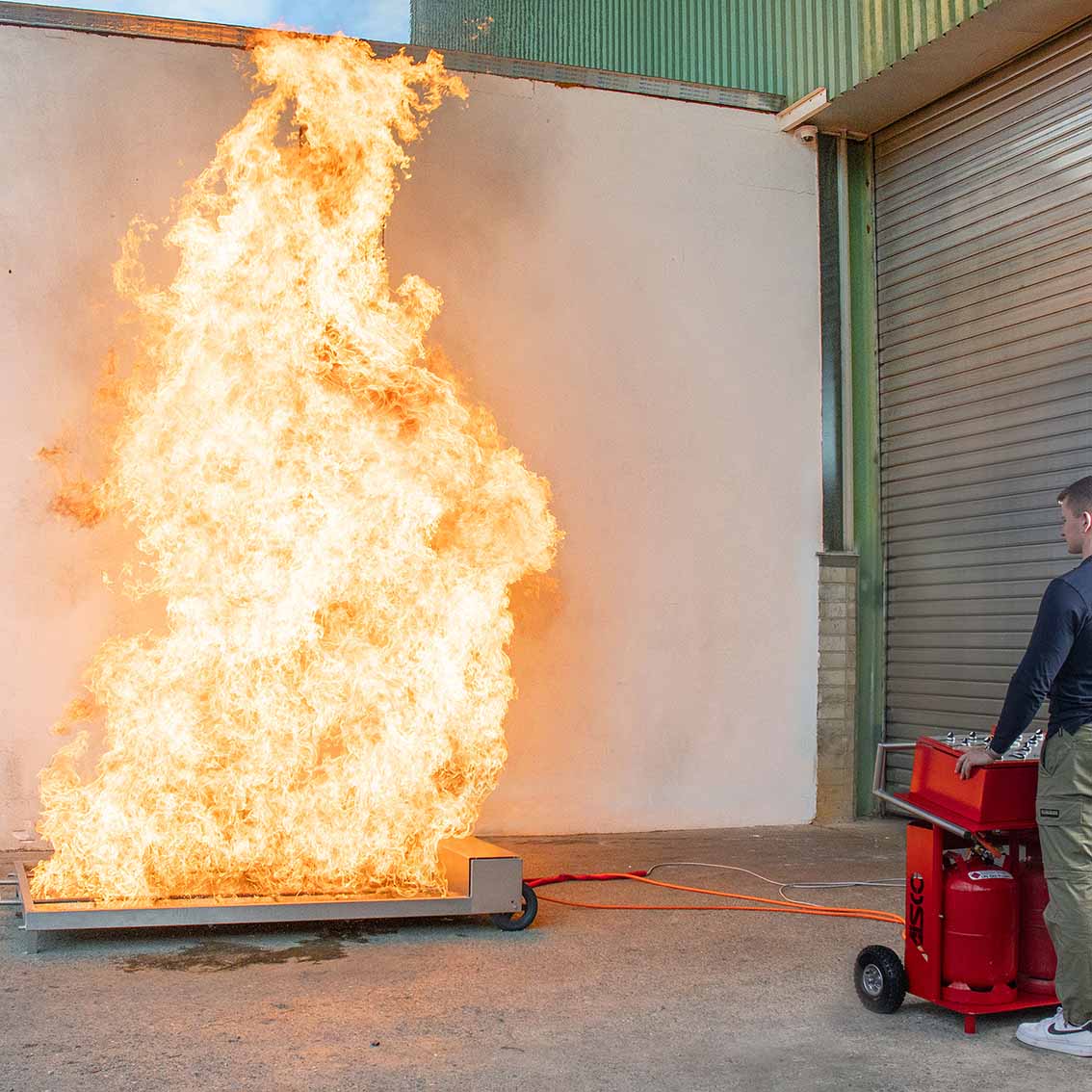 AISCO Firetrainer E1502 XL Brandsimulator im Live-Einsatz mit meterhohen Flammen und sichtbarem Bedienpult für kontrolliertes Feuerwehrtraining