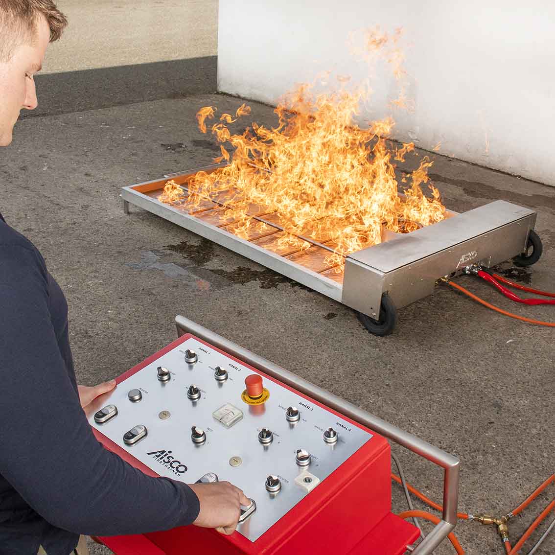 AISCO Firetrainer E1502 XL Brandsimulator im realitätsnahen Live-Einsatz mit brennendem Flächenbrand; Schaltfläche des Bedienpults zur Steuerung des Brandgeschehens deutlich erkennbar