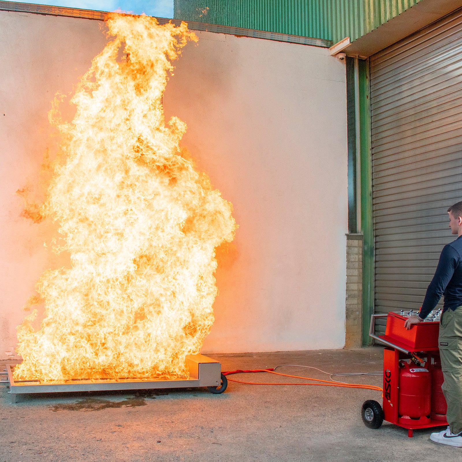 AISCO Firetrainer E1502 XL fire simulator in live operation with meter-high flames and visible control panel for controlled firefighter training