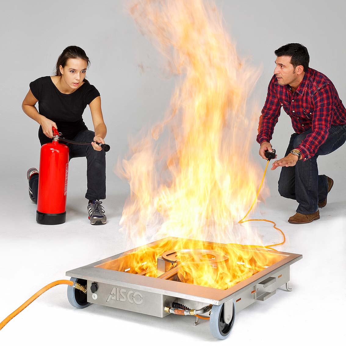 AISCO Firetrainer E 100 brennend, una Person löscht il/la Feuer, während il Brandschutzhelfer Anweisungen gibt