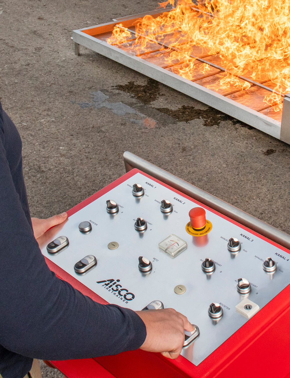 Feuerwehrkraft bedient Steuerpult F4, im Hintergrund brennender Firetrainer E1502XL